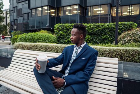 African American businessman wearing blue suit drinks coffee near officeの写真素材