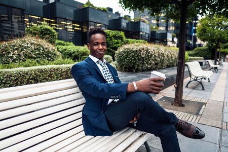 African American businessman wearing blue suit drinks coffee near officeの写真素材