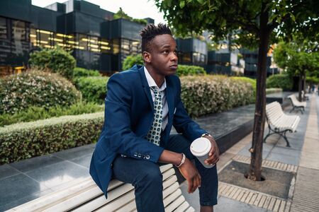 African American businessman wearing blue suit drinks coffee near officeの写真素材