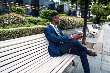 African American businessman wearing blue suit drinks coffee near officeの写真素材