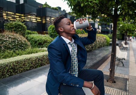African American businessman wearing blue suit drinks coffee near officeの写真素材