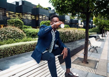 African American businessman wearing blue suit drinks coffee near officeの写真素材