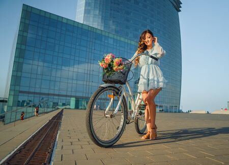 Asian model in a blue dress rides a white bicycle in a green parkの写真素材