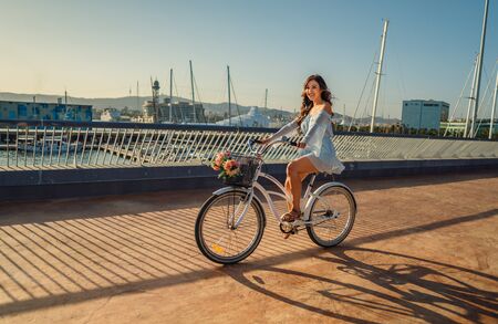 Asian model in a blue dress rides a white bicycle in a green parkの写真素材