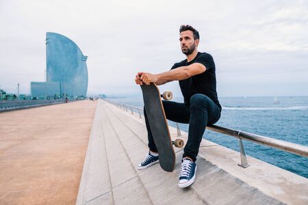 Skateboarder sits with skateboard on the modern city sea terraceの写真素材