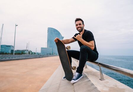 Skateboarder sits with skateboard on the modern city sea terraceの写真素材