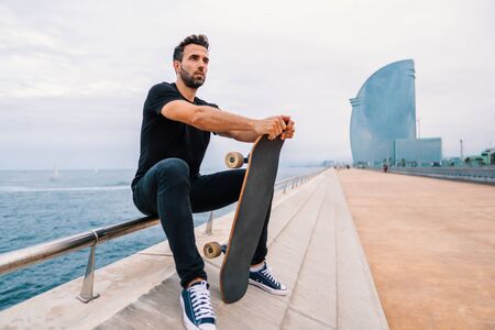 Skateboarder sits with skateboard on the modern city sea terraceの写真素材
