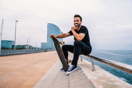 Skateboarder sits with skateboard on the modern city sea terraceの写真素材