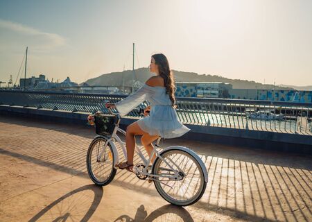 Asian model in a blue dress rides a white bicycle in a green parkの写真素材
