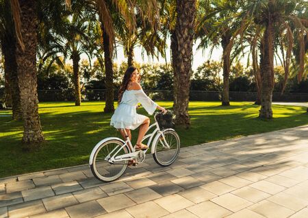 Asian model in a blue dress rides a white bicycle in a green parkの写真素材