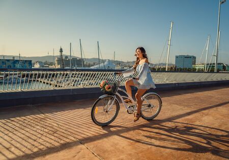 Asian model in a blue dress rides a white bicycle in a green parkの写真素材