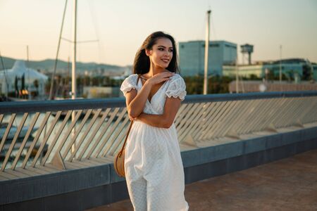 Beautiful girl in the white dress walking along the sea promenadeの写真素材