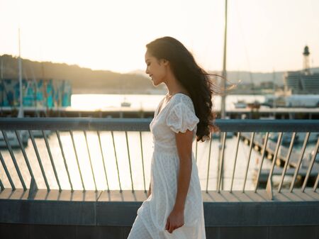 Beautiful girl in the white dress walking along the sea promenadeの写真素材