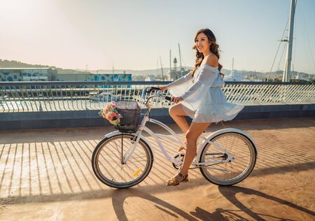 Asian model in a blue dress rides a white bicycle in a green parkの写真素材