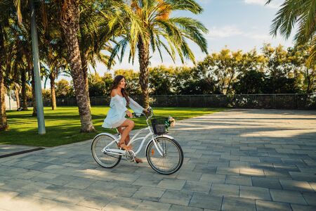 Asian model in a blue dress rides a white bicycle in a green parkの写真素材