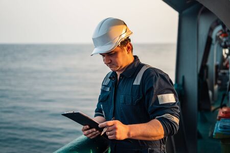 Deck Officer on deck of offshore vessel or ship , wearing PPE personal protective equipment. He fills checklist. Paperwork at seaの写真素材