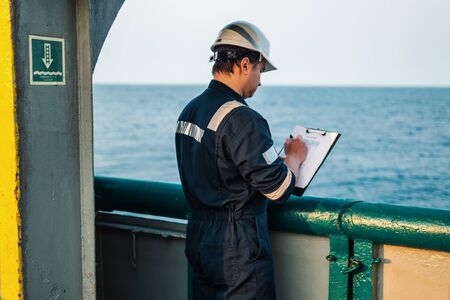 Deck Officer on deck of offshore vessel or ship , wearing PPE personal protective equipment. He fills checklist. Paperwork at seaの写真素材