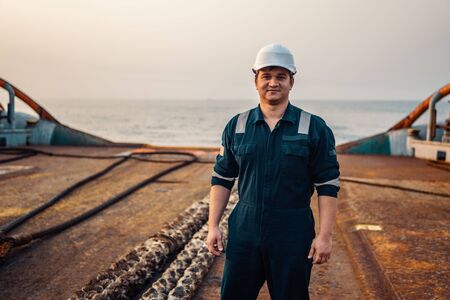 Marine Deck Officer or Chief mate on deck of offshore vessel or ship , wearing PPE personal protective equipment - helmet, coverall. He holds VHF walkie-talkie radio in hands.の写真素材