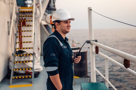 Marine Deck Officer or Chief mate on deck of offshore vessel or ship , wearing PPE personal protective equipment - helmet, coverall. He holds VHF walkie-talkie radio in hands.の写真素材