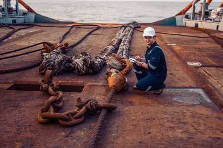 Marine chief officer or chief mate on deck of ship or vessel. He fills up ahts vessel checklist. Ship routine paperwork. He holds VHF walkie-talkie radio in hands.の写真素材