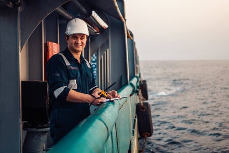 Deck Officer on deck of offshore vessel or ship , wearing PPE personal protective equipment. He fills checklist. Paperwork at seaの写真素材