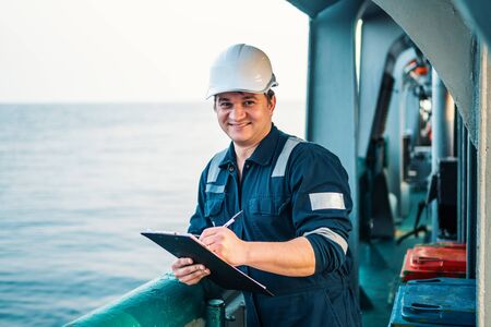 Deck Officer on deck of offshore vessel or ship , wearing PPE personal protective equipment. He fills checklist. Paperwork at seaの写真素材