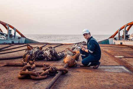Marine chief officer or chief mate on deck of ship or vessel. He fills up ahts vessel checklist. Ship routine paperwork. He holds VHF walkie-talkie radio in hands.の写真素材