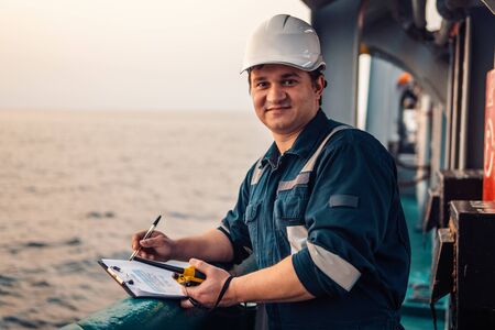 Deck Officer on deck of offshore vessel or ship , wearing PPE personal protective equipment. He fills checklist. Paperwork at seaの写真素材