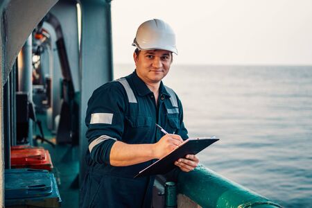 Deck Officer on deck of offshore vessel or ship , wearing PPE personal protective equipment. He fills checklist. Paperwork at seaの写真素材