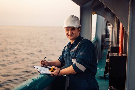 Deck Officer on deck of offshore vessel or ship , wearing PPE personal protective equipment. He fills checklist. Paperwork at seaの写真素材