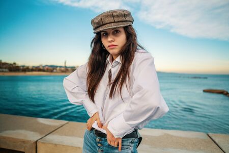 Portrait of young beautiful stylish woman in white shirt and grey capの写真素材