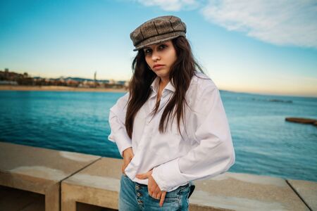 Portrait of young beautiful stylish woman in white shirt and grey capの写真素材