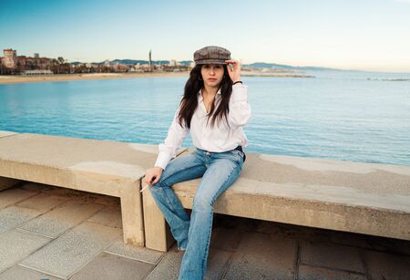 Portrait of young beautiful stylish woman in white shirt and grey capの写真素材