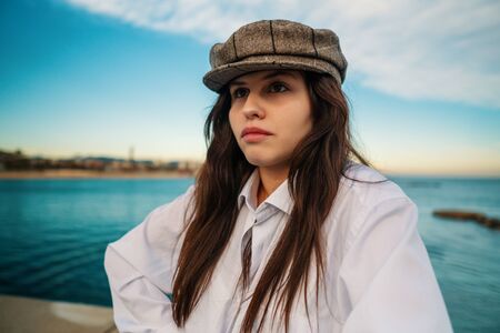 Portrait of young beautiful stylish woman in white shirt and grey capの写真素材