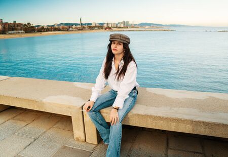 Portrait of young beautiful stylish woman in white shirt and grey capの写真素材