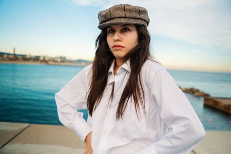 Portrait of young beautiful stylish woman in white shirt and grey capの写真素材