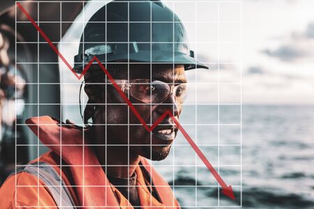 Concept of falling market in marine industry with downward graphics. Seaman AB or Bosun on deck of vessel or ship , wearing PPE.の写真素材