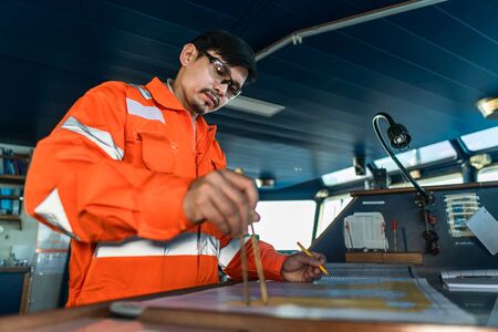 Filipino deck Officer on bridge of vessel or ship. He is plotting position on chartの写真素材