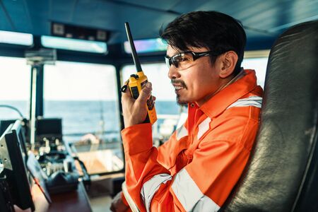 Filipino deck Officer on bridge of vessel or ship. He is speaking on GMDSS VHF radioの写真素材
