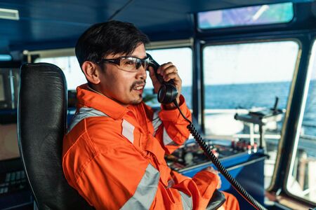 Filipino deck Officer on bridge of vessel or ship. He is speaking on GMDSS VHF radioの写真素材