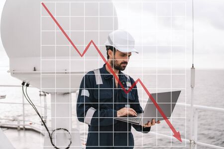Concept of falling market in marine industry with downward graphics. Service technician or serviceman near VSAT terminalの写真素材