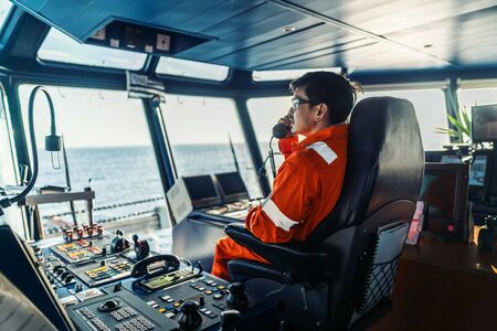 Filipino deck Officer on bridge of vessel or ship. He is speaking on GMDSS VHF radioの写真素材