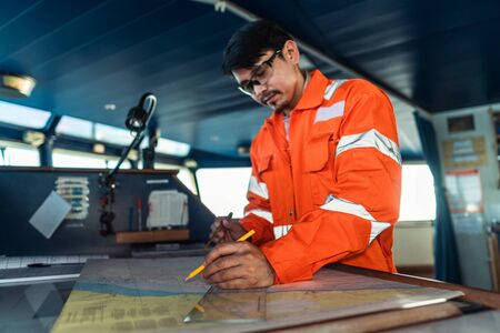 Filipino deck Officer on bridge of vessel or ship. He is plotting position on chartの写真素材
