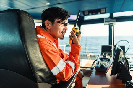 Filipino deck Officer on bridge of vessel or ship. He is speaking on GMDSS VHF radioの写真素材