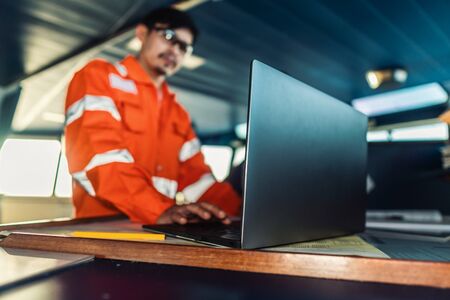 Filipino deck Officer on bridge of vessel or ship. He is using laptop, electronic paperwork at seaの写真素材