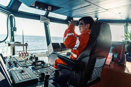 Filipino deck Officer on bridge of vessel or ship looking through binocularsの写真素材