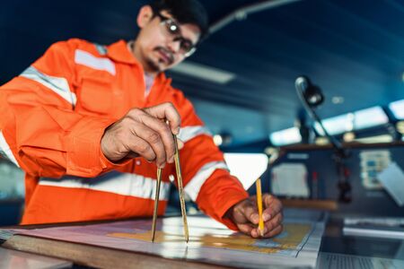 Filipino deck Officer on bridge of vessel or ship. He is plotting position on chartの写真素材