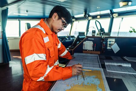 Filipino deck Officer on bridge of vessel or ship. He is plotting position on chartの写真素材
