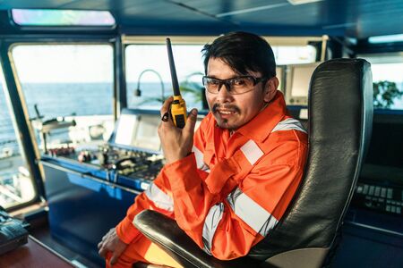 Filipino deck Officer on bridge of vessel or ship. He is speaking on GMDSS VHF radioの写真素材