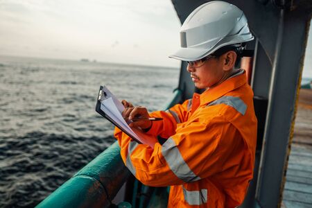 Filipino deck Officer on deck of offshore vessel or ship fills checklist. Paperwork at seaの写真素材
